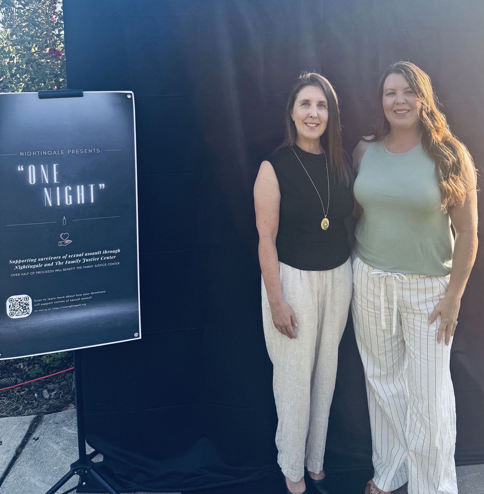 Two organizers stand beside the One Night event sign.