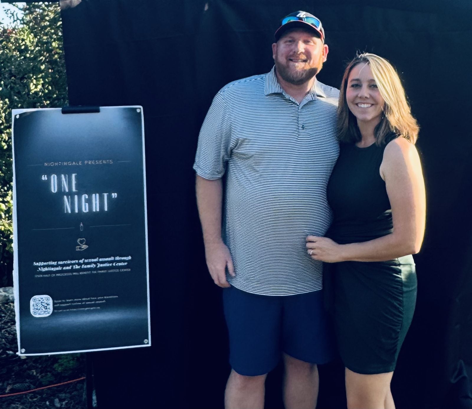 A couple stands beside the One Night event sign.